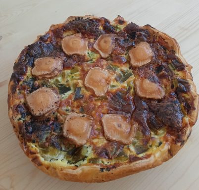 Tarte salée garnie de morceaux de viande et de légumes, avec une croûte dorée.